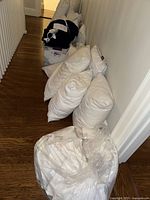 White bed pillows and sheets in bins arranged on the floor showing quantity and condition.