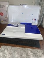 White portable desk open with USB charger, blue trays, whiteboard markers, and charging cable visible.