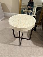 Round white mosaic tile-style top table with black metal base photographed from an angle, showing design and structure.