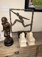 Full view of the bronze basketball player sculpture, bronze hurdle jumper sculpture in rectangular frame on marble base, and two stone lion statues on rectangular pedestals on a wooden table.