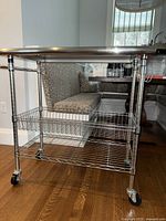 Stainless steel kitchen cart from an angle showing lower wire baskets and wheels