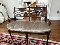 Front view of two-seat carved wooden bench with cane back and silk cushion