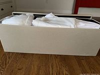 Fabric storage container filled with folded white and beige linens