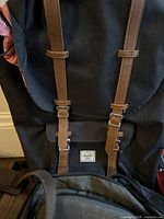 Close-up of black Herschel backpack with brown leather straps and buckle details