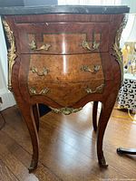 Ornate footed chest side table front view showcasing wood veneer and decorative metal hardware with three drawers and curved legs.