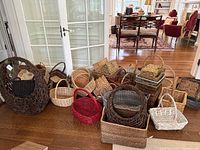 Overview image showing a large assortment of baskets grouped on the floor, showcasing different colors and sizes from large dark brown open weave to natural wicker and painted options.