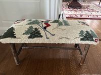 Front view of the small bench showing the embroidered seat with skier figures and twig-style legs.