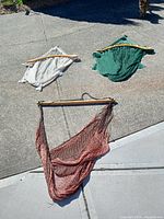 Three netted hammock chairs in white, green, and brown colors laid out on concrete surface.