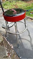 Full view of Fender bar stool showing padded black and red seat with chrome base on outdoor surface