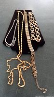 Four necklaces laid on black velvet showing variety in style and chain type. Included rhinestone necklace and three gold tone necklaces of varying widths.