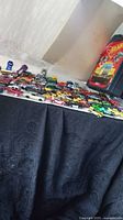 Wide shot of approximately 40 Hot Wheels toy cars in various colors and styles, laid out on a black patterned cloth.
