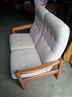Front-side angled view of beige tufted loveseat with wooden armrests and frame, showing attached seat and back cushions.