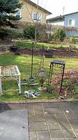 Wider view of all items grouped together on lawn including plant bench, garden obelisk, hanging lantern, metal tree wall art, garden stakes, and plant stands.