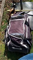 Photo showing large dark-colored sports bag with wheels on the ground next to baseball equipment, depicting size and condition.