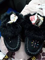 Photo showing pair of black suede moccasins with black fur collar and colorful beadwork on toes, stuffed with newspaper to keep shape.
