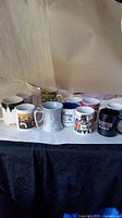 Photo showing 10 assorted mugs in different designs and colors arranged on a white surface with black table below.