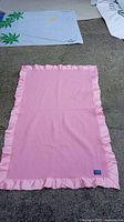 Full view of the pink wool blanket with ruffled satin edges laid flat.