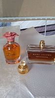 Three perfume bottles displayed on white surface, including Dolce by Valentino with pink rose cap, Marc Jacobs Decadence, and a small mini bottle