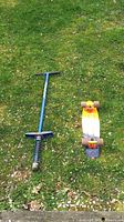 Blue pogo stick and vintage skateboard side by side on grass