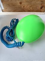 Side view of green oval UFO-shaped lamp with blue coiled cord and plug