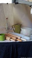 Full view of kitchen set showing all items: two jugs, green mug, butter churn, and four rolling pins on a white surface with neutral background.