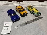 Photo showing three display model cars: a blue 2000 Chevy SSR, a yellow and black Maisto Hummer H2, and a yellow and green 1930 Duesenberg with cloth top, ruler included for scale.