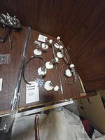 Photo of bathroom hardware set on wooden surface showing curved towel bars, toilet paper holder, robe hooks, and grab bar with white ceramic and chrome finish.