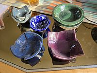 Various views of six handmade ceramic small bowls in different colors and shapes displayed on a reflective surface under natural light.