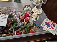 Wide view of box containing ribbons, bows, ornaments, figurines, holly sprigs, and snowflake decorations arranged together