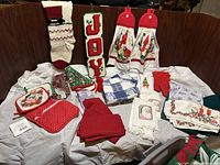 Full display of Christmas kitchen textiles: pot holders, towels, decorative stockings, oven mitts, napkins, and decorative JOY blocks.