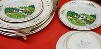 Stack of Newcor dinner and dessert plates showing colorful rural farm landscape and cherry border pattern, one plate turned to show base stamp.