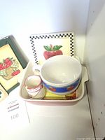 Photo showing apple themed small ceramic bowl, mini pitcher, rectangular dish, and square decorative trivet featuring a large apple with a checkered border.