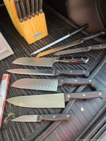 Seven Farberware knives (scalloped, serrated, chef's, utility) and sharpening steel laid adjacent to wooden cutlery block with Farberware brand