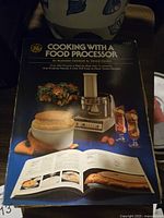 Photo of the GE 'Cooking with a Food Processor' cookbook showing cover with food processor and food images.