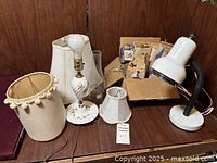 Photo of lamps, lampshades, and box of assorted light bulbs and lamp parts on wooden surface.