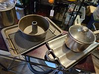 Metal Bundt pan, roasting pans and Farberware lobster pot with glass lid on metal table