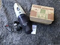 Lot contents showing Micronta Power Inverter in original box next to Black & Decker Dust Buster vacuum and charger on a carpet surface.