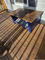 Rectangular coffee table with natural wood top and blue painted base on a wooden deck.