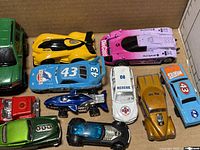 Top-down view of toy cars and trucks in a box showing a variety of vehicles including race cars, trucks, motorcycles, and a bus.