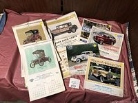 Full lot of vintage car calendars from the 1970s showing early 20th century car images spread out on a table