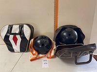 Two bowling balls positioned side by side with their respective carry cases, one black and white and one brown, showing overall condition and style.