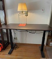 Front view of the AIRLIFT S3 adjustable standing desk with walnut surface and black legs, showing control panel on right side and wall lamp above.