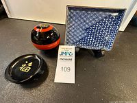 Vintage Japanese black lacquer round container with lid, 6 matching coasters, and Fitz and Floyd blue mosaic pattern tray displayed on a black surface.