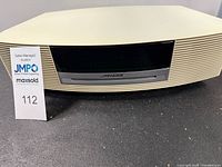 Front view of beige Bose Wave Music System with paper auction tag 112 in front.