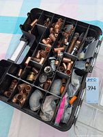 Photo of open black plastic double-sided organizer box filled with assorted copper plumbing fittings segmented by compartments