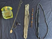 Top view of seven items laid on a dark fabric including the Versace perfume bottle, multiple necklaces, rings, and a bracelet.