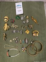 Full layout of the lot with assorted costume pins, bracelets, rings, and pendants arranged on green fabric.