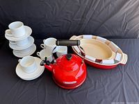 Set showing eight white cups and saucers arranged beside red Le Creuset tea kettle and oval baking dishes.
