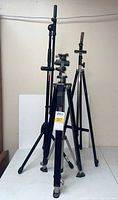 Photo of three black metal stands including one easel and two tripods against white background, showing general setup and condition.