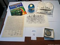 Top-down photo showing the full lot items on white surface: book titled 'Solutions', vintage small globe bank, sealed NAS t-shirt, Declaration reproduction document, drawing of San Francisco skyline, commemorative coin in box